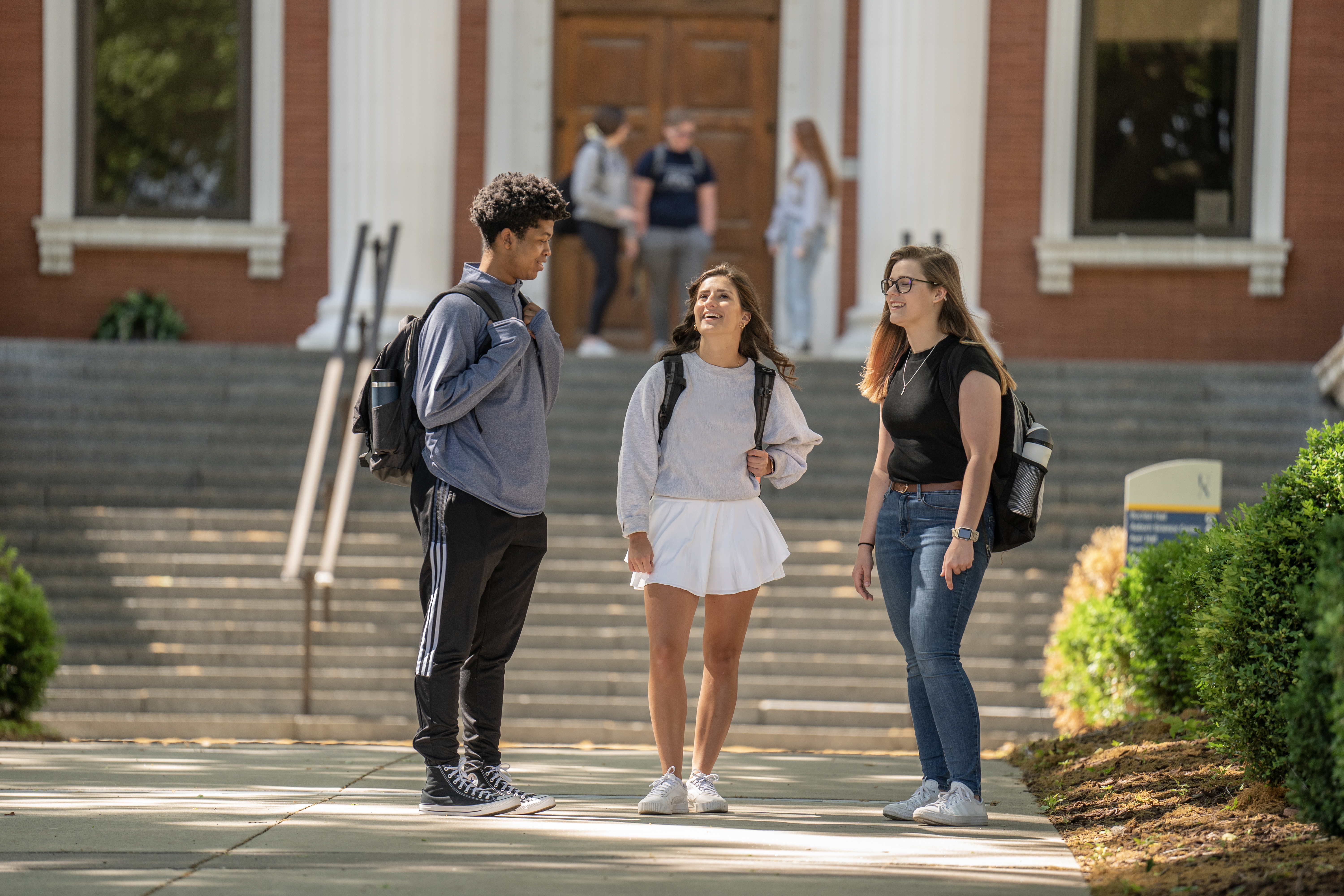 Three students talking with Buchtel Hall in the background